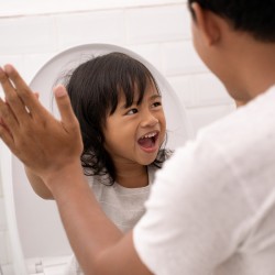 Smiling toddler girl on toilet and shoulder and arm view of father who is high fiving her