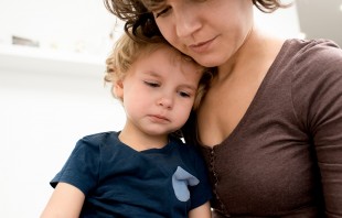 Mother wearing brown shirt comforting sniffling toddler boy on her lap