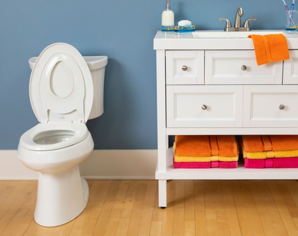 LIttle2Big built-in potty seat on toilet next to white vanity with orange, yellow and red towels on a shelf