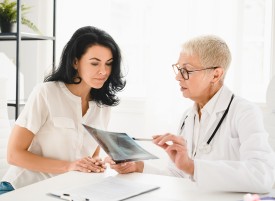 Female doctor discussing medical image with younger female patient with long brown hair.