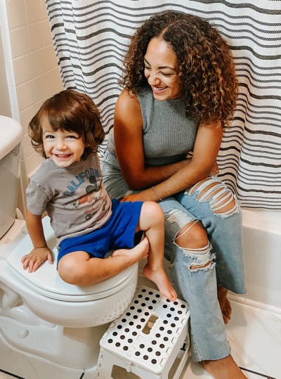 Mother sitting on tub in bathroom with smiling toddler son sitting on toilet