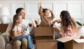 Family on couch with small girl sitting on father's lap and another happy girl sitting in a cardboard box