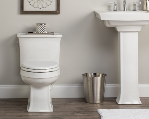 Bathroom setting showing white toilet, silver garbage can and white pedestal sink