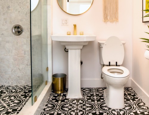 Modern bathroom with black patterned floor, Bemis toilet seat with black hinges next to a white pedestal sink