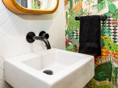 Square white bathroom sink with black faucet and green patterned shower curtain