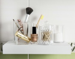 Shelf with small plastic containers filled with brushes, eyelash curler, nail polish and cotton swabs