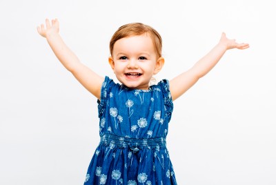 Smiling little girl wearing blue dress holds both arms up in celebration